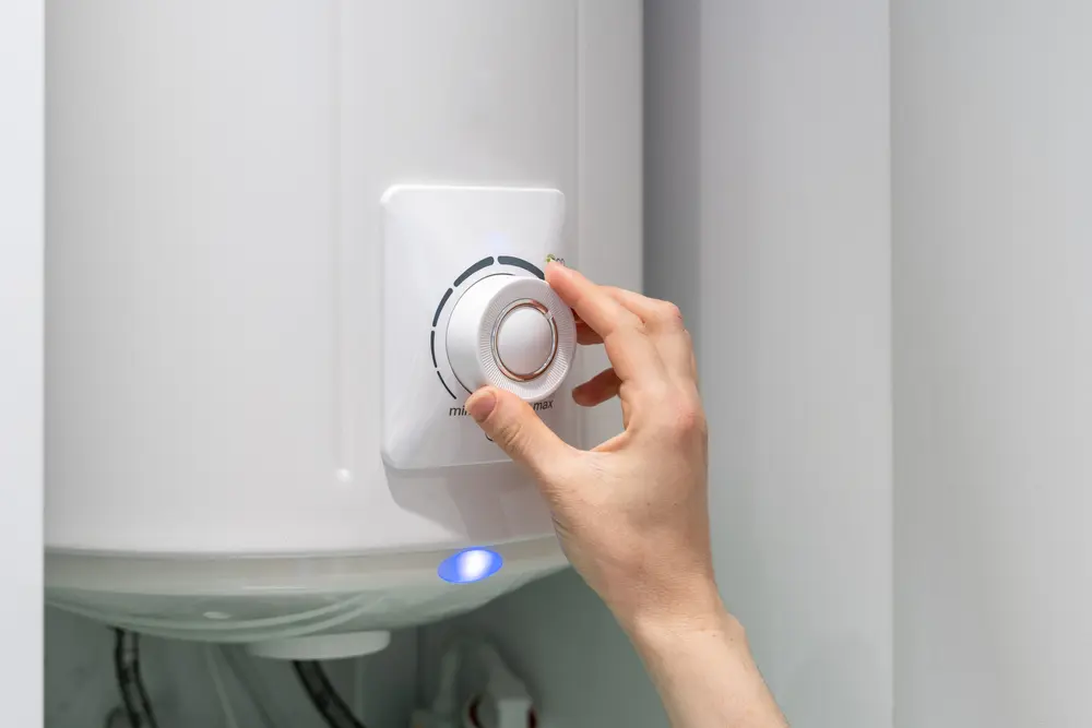 Cropped photo of female adjusting temperature on bathroom electric boiler hanging on wall, using control knob. Water heater in modern apartment