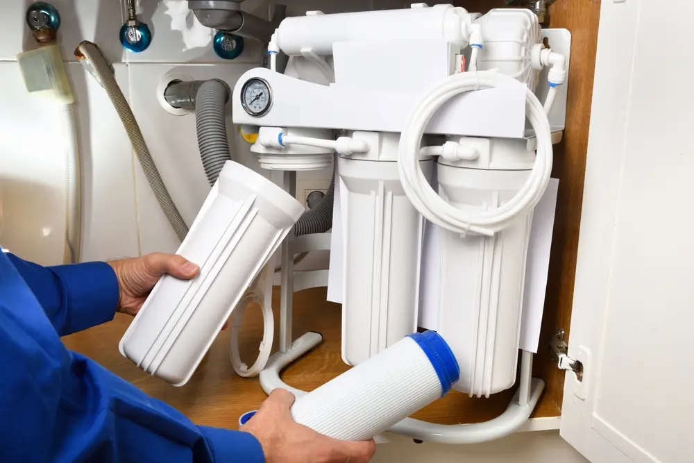 plumber installing reverse osmosis equipment under the sink close up. Front view. Horizontal composition.