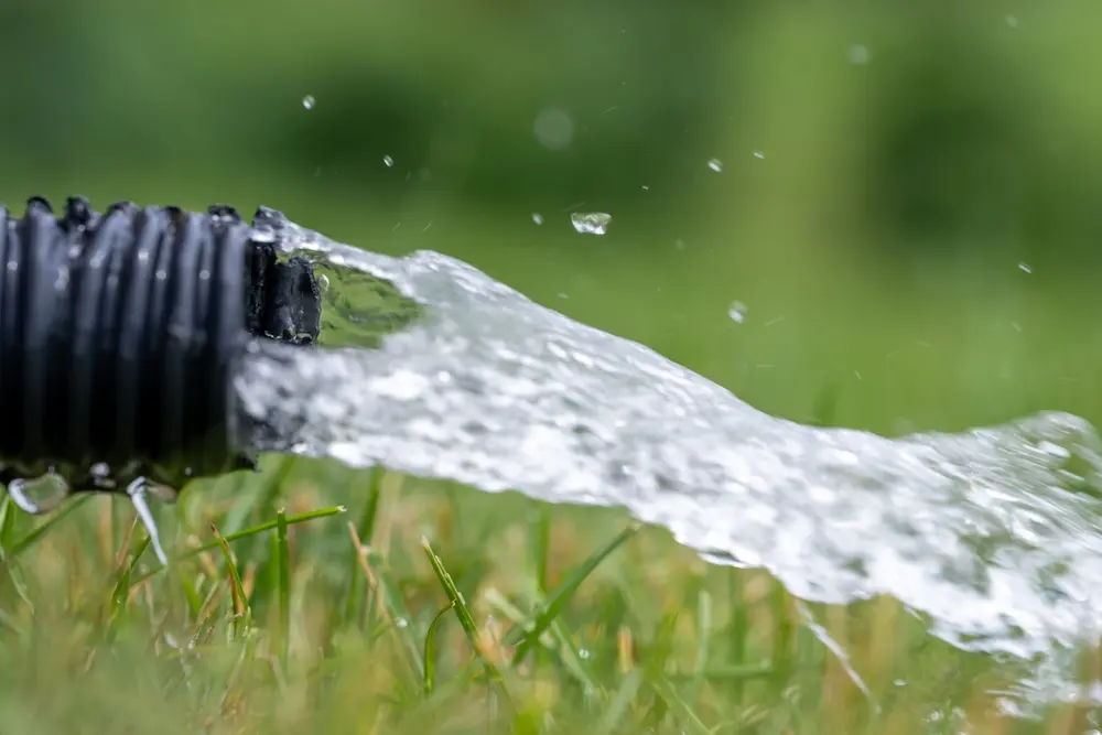 Residential sump pump drain line discharging water into grass yard after a rainstorm